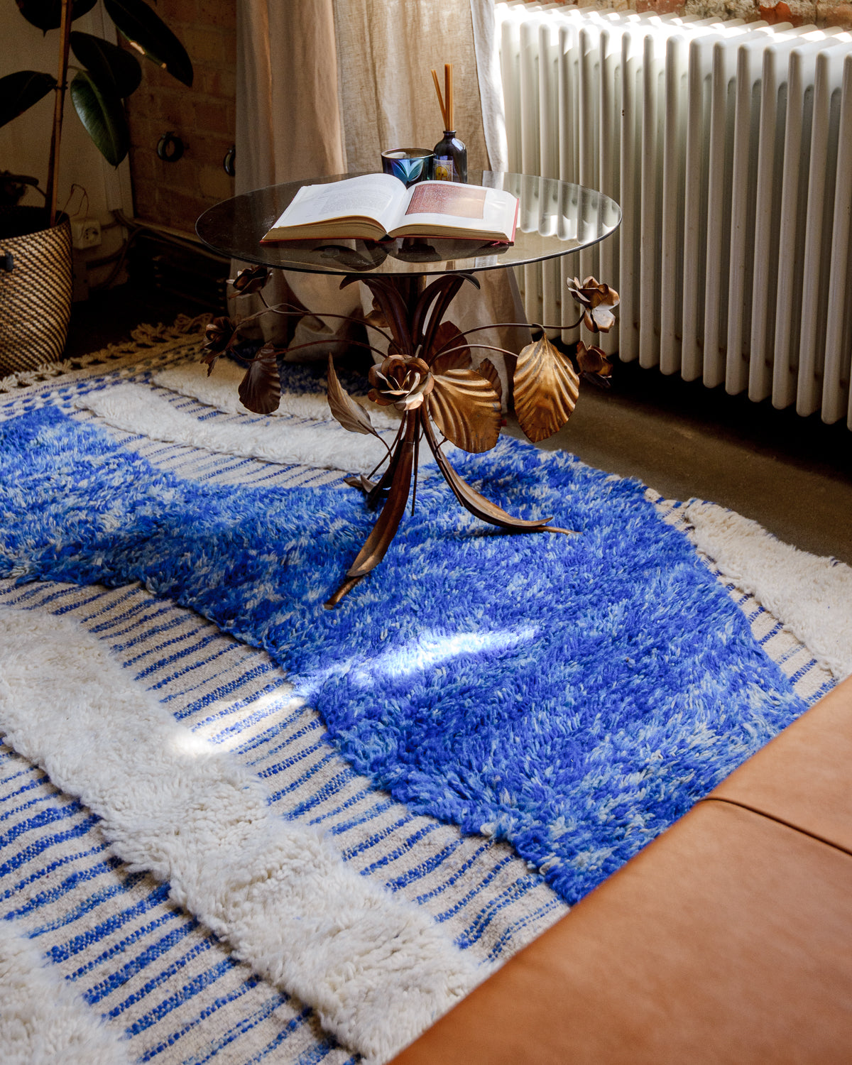 Blue and cream Berber rug in a quiet corner scene with an art deco coffee table, cream linen curtain and leather couch.